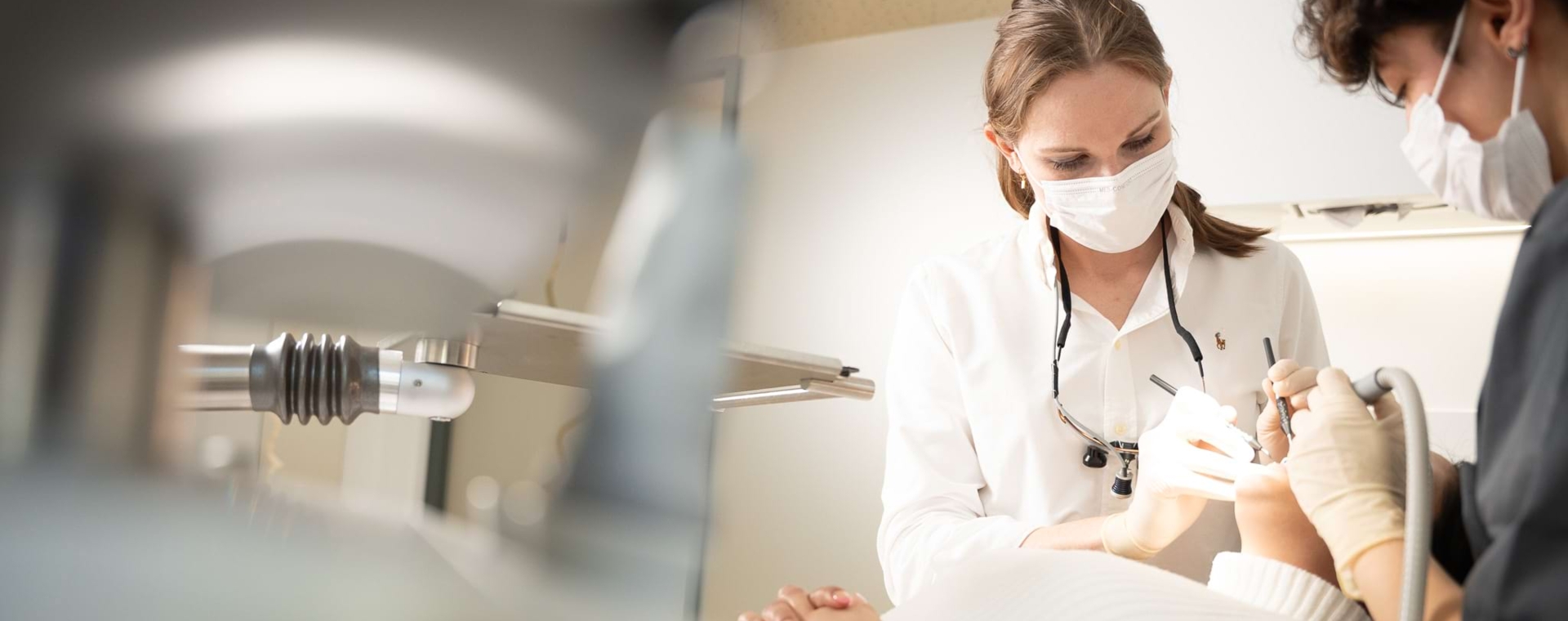 Eine Zahnärztin und Assistenz bei einer oralchirurgischen Behandlung einer Patientin, die mit offenem Mund auf dem Behandlungsstuhl liegt