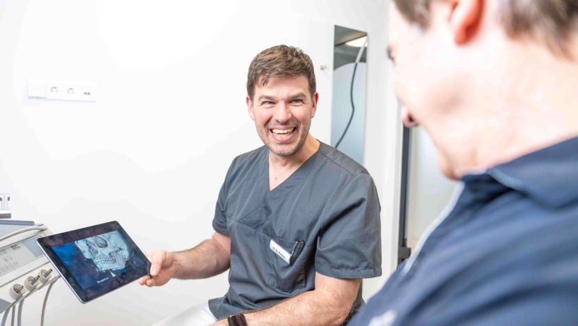 Dr. med. Dr. med. dent. Steffen Kargus (links) lacht und zeigt Dr. med. Dr. med. dent. Alfred Hertler (rechts) eine Aufnahme