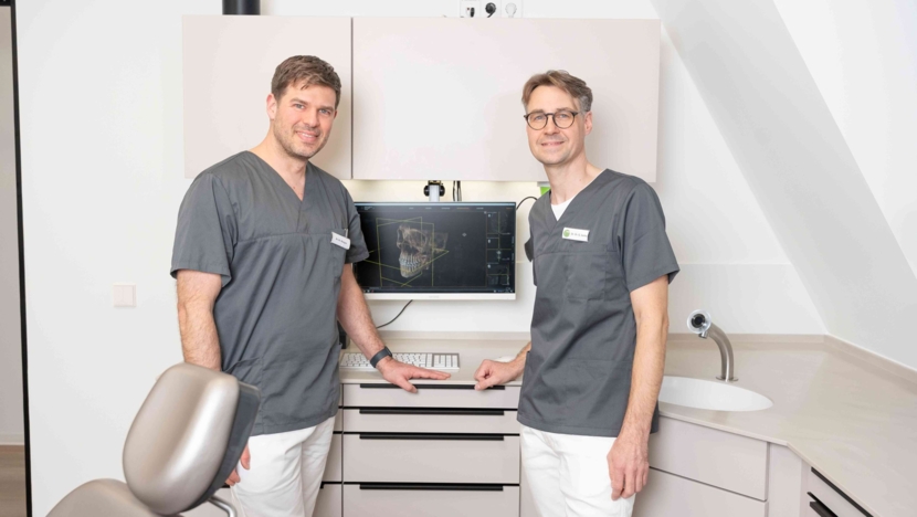 Dr. Dr. Kargus und Dr. Dr. Santo stehen vor der technischen Ausstattung eines Behandlungszimmers und tauschen sich aus
