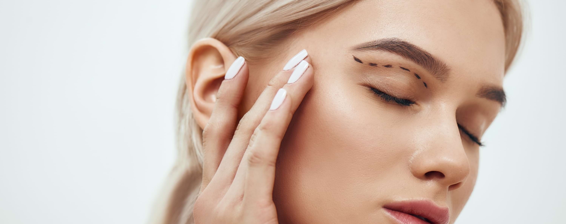 Beautyshot einer blonden Frau, die am Oberlied Markierungen für einen Eingriff der Lidstraffung eingezeichnet hat