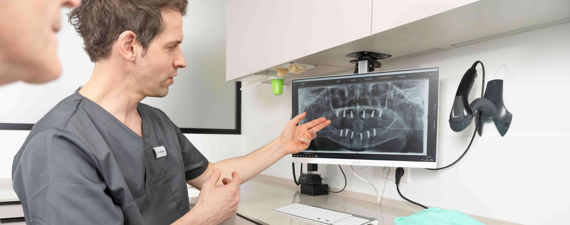 Dr. Elsäßer erklärt einem Patienten die Lage seiner Implantate im Kiefer anhand eines digitalen Röntgenbildes